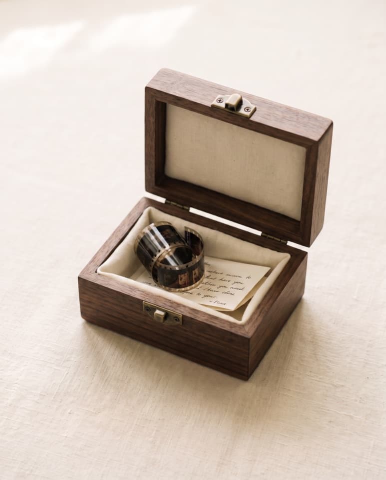 An open walnut keepsake box holding a rolled strip of film and a handwritten note